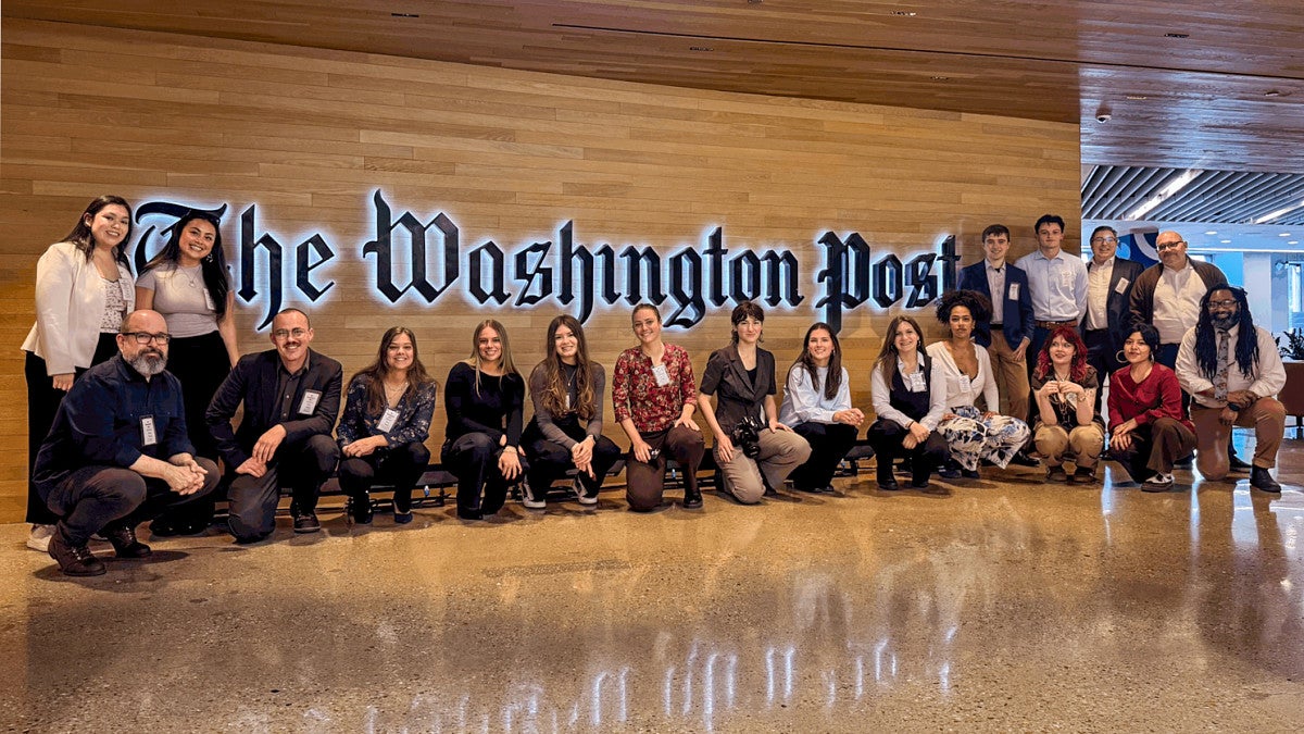 Several people pose in front of a wood wall with a large sign for the The Washington Post