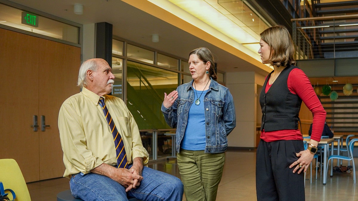 Dan Morrison, Lori Shontz, and Julia Boboc have a discussion in the atrium of Allen Hall on the University of Oregon campus