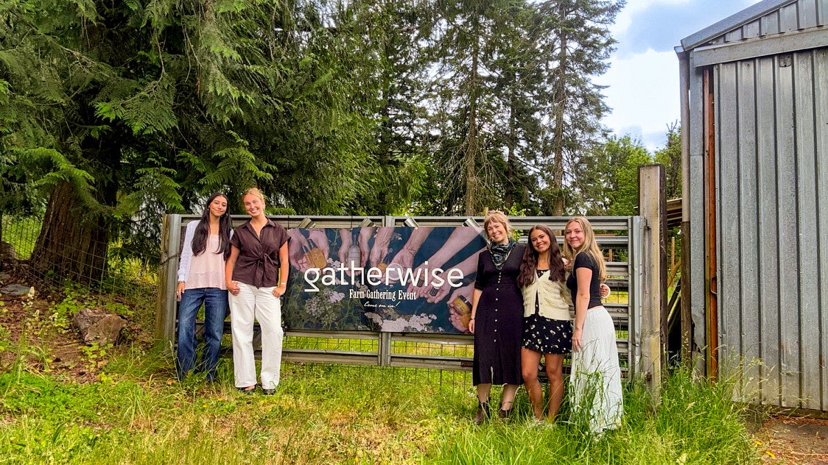 five women pose in front of a banner hung on a farm gate