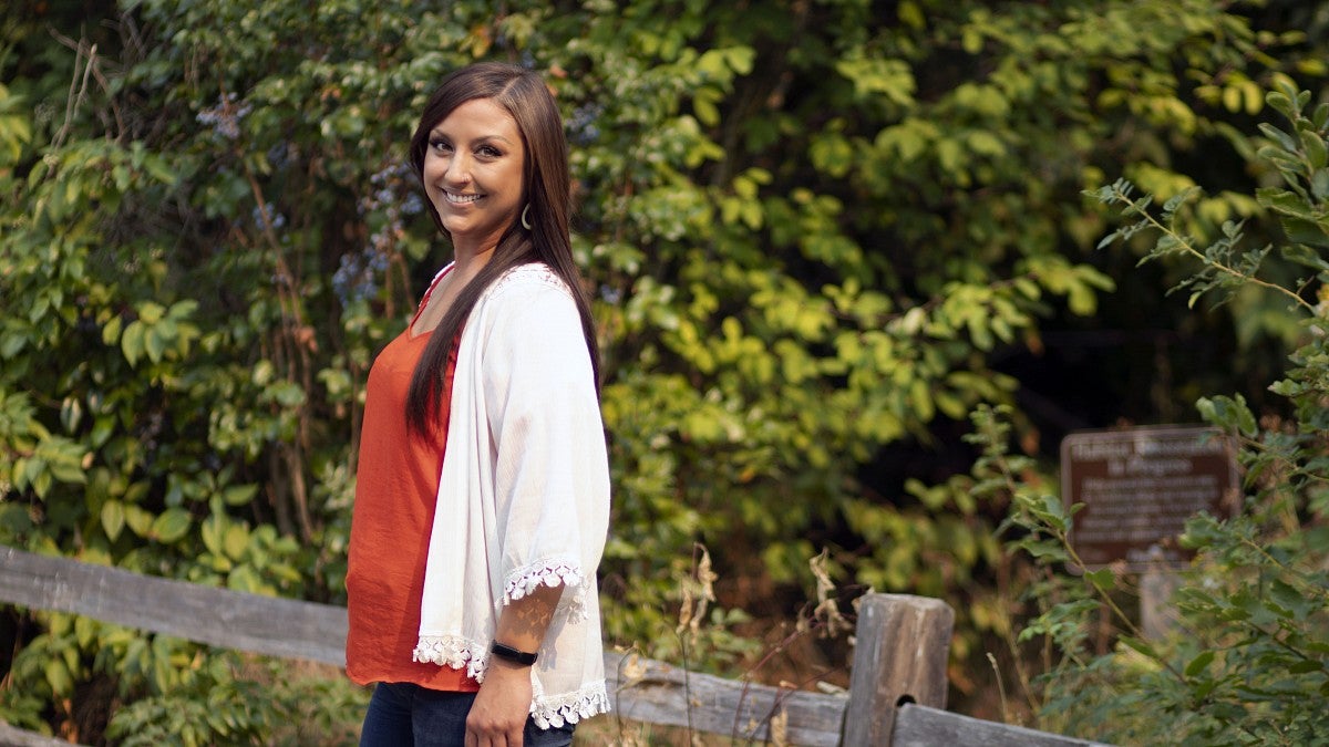 Whitney Gomes smiles while standing on a bridge in a forest