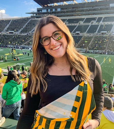 Jillian Gray wears yellow and green striped overalls at Autzen Stadium during a UO football game