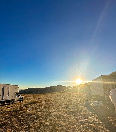view of production trucks in a field looking towards the sun rising over hills
