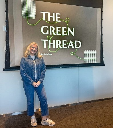 Catie Foley stands in front of a screen displaying the title of her Advertising and Brand Responsibility master's capstone project called "The Green Thread"