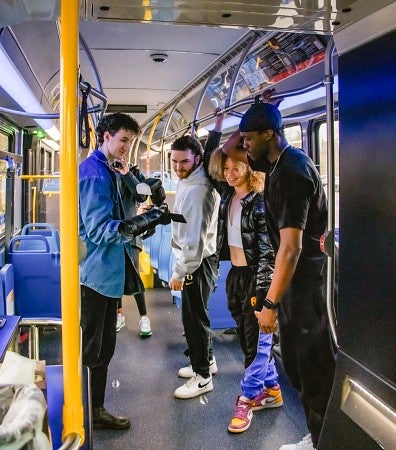 a student photographer shows three student athletes the back of his camera during a photo shoot on board a bus