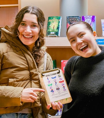 two members of the SOJC PR student competition team hold up a colorful scavenger hunt list