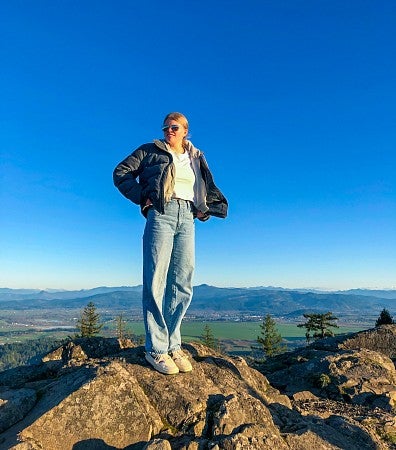 Annika Nagat standing on a rock with a vibrant blue sky covering most of the background
