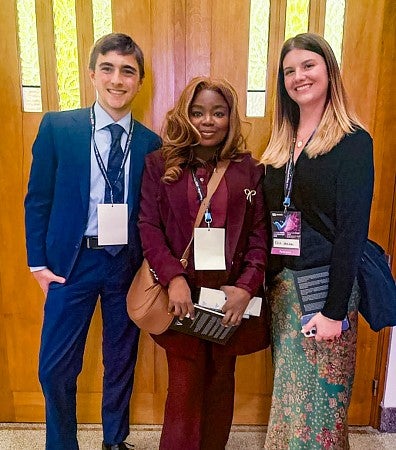 three people pose for a photo in front of double doors with stained glass inserts