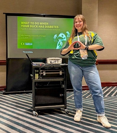 Ally Thomas throws her O in front of a digital screen showing a presentation about supporting University of Oregon community members with diabetes