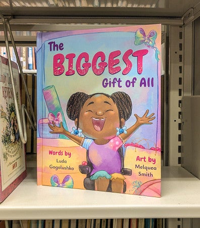 a colorful children's book titled "The Biggest Gift of All" sits on a library shelf