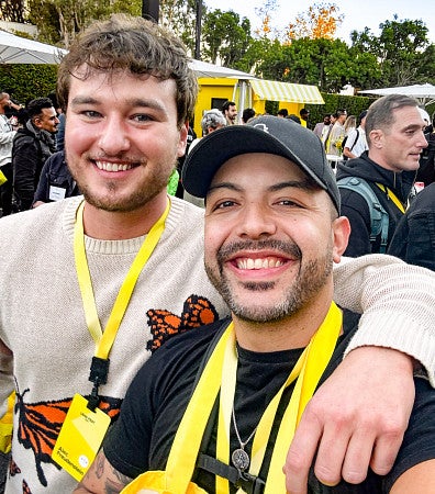 Alec Freudenstein with his arm around Danny Pimentel at an outdoor party; they both have bright yellow lanyards on