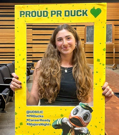 Elizabeth Weltzien poses with a yellow cardboard cutout frame that says "Proud PR Duck"