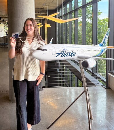 Maya Valverde holds up her Alaska Airlines internship badge while posing next to a model airplane