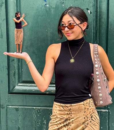 Kaia Mikulka looks at her outstretched hand where a smaller, AI-generated version of herself stands and waves at her