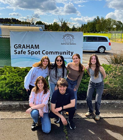 a group of public relations students posing outside in front of a safe spot community banner