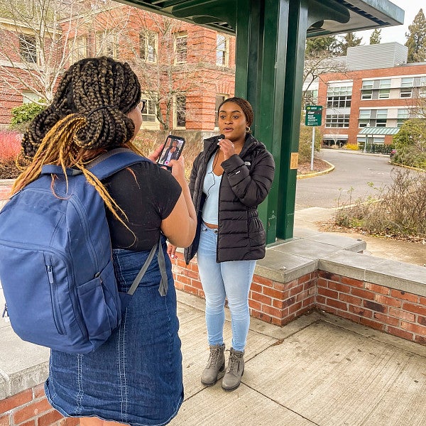 a student uses an iphone to film another student speaking into a microphone