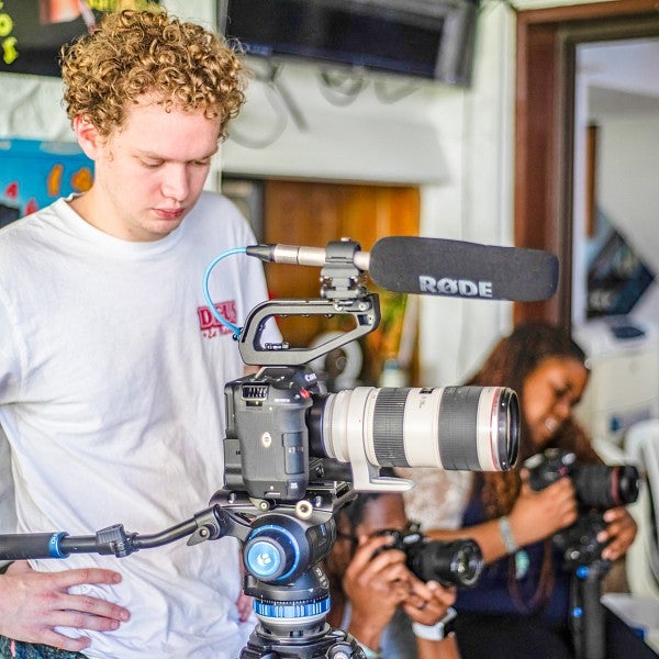 Brady Doran stands behind a video camera on a tripod