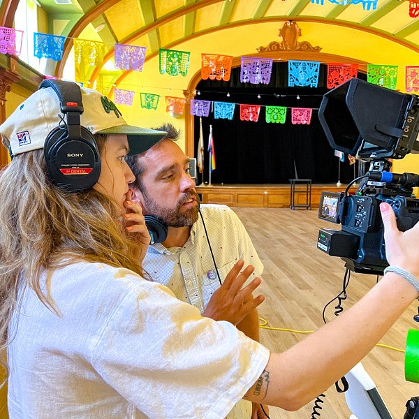 two people look into the back of a video camera in a bright yellow room with vibrant paper flags