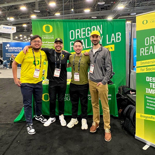 four people pose in front of a vibrant green and yellow trade show display for the Oregon Reality Lab
