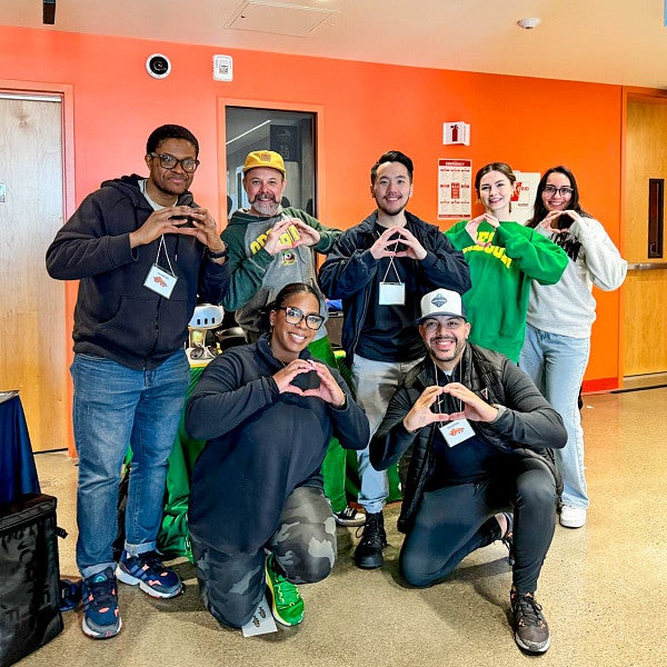a group of students and a professor from the University of Oregon Immersive Media Communication Master's program pose while holding their hands in the shape of Os