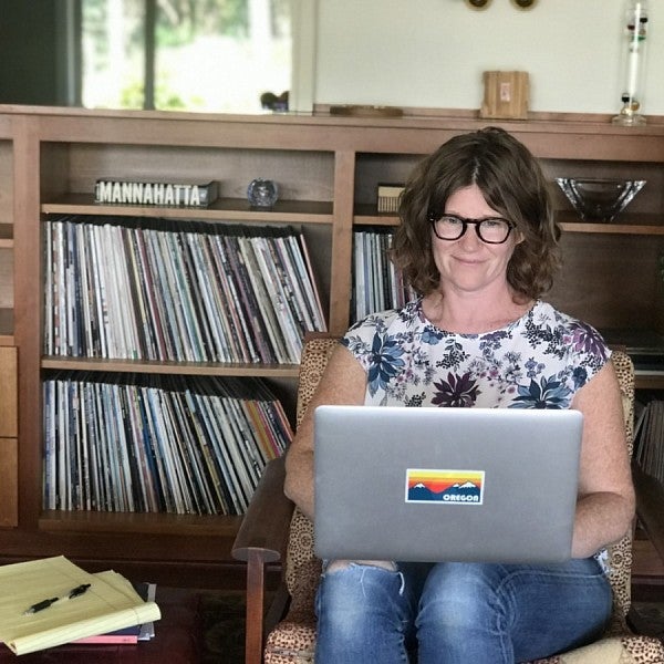 Kathryn Kuttis types on her grey laptop with an Oregon sticker in front of a record shelf.