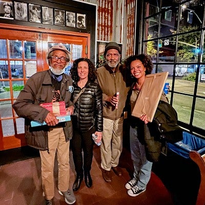 four people pose in front of a large window and door