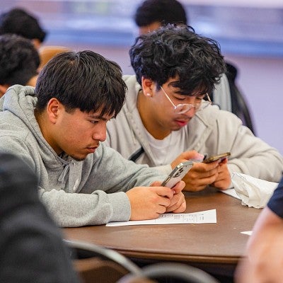 two highschool students use their cell phones to take a survey about local news and information