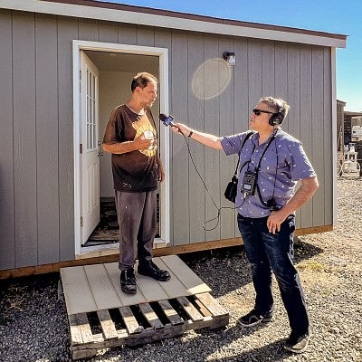 Brian bull audio records an interview with a person standing in the doorway of a tiny house