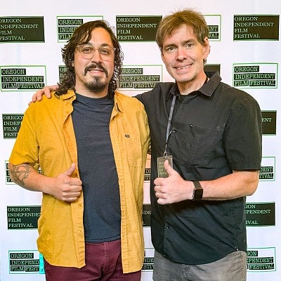 J.J. Kirby and Kelly Clendenon pose in front of a white backdrop with logos for the Oregon Independent Film Festival
