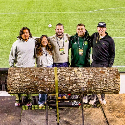 five people stand behind a large section of a log 