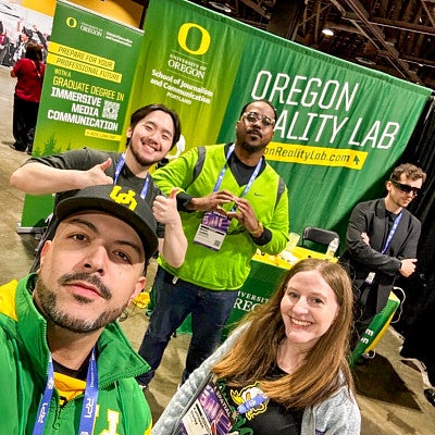 The Oregon Reality Lab team poses in front of their vibrant green and yellow booth at an augmented reality expo