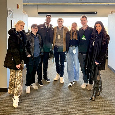 a group of people wearing press passes pose inside a football stadium media room