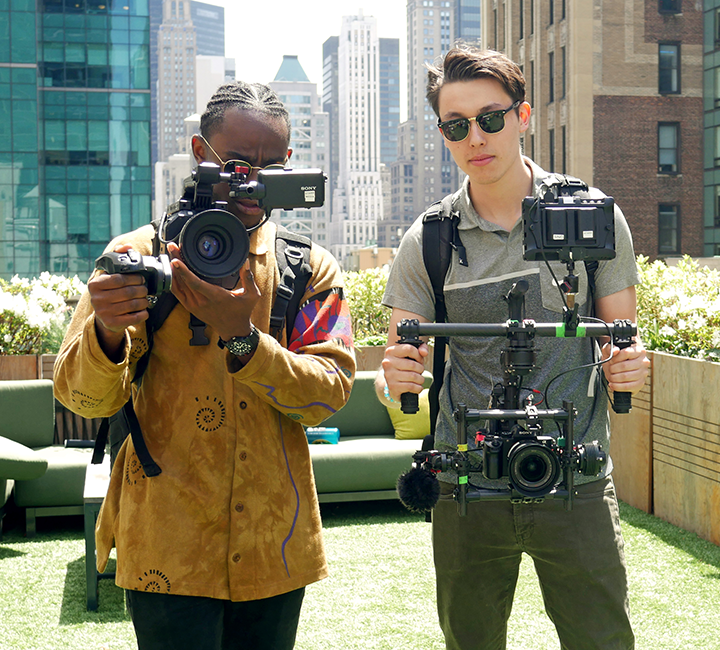 two SOJC students with camera equipment film on an outdoor rooftop in a city setting