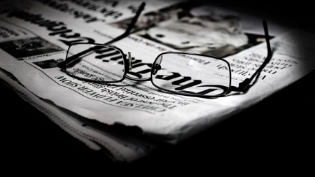 A pair of reading glasses placed on top of a black and white newspaper.