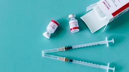Two vials of the COVID-19 vaccine and a syringe on a teal surface (Pexels).