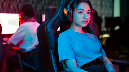 A woman in blue shirt sits in a black and red gaming chair (By Ron Lach from Pexels).