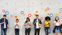 Six young adults look at their smart phones, with various emojis in the background.