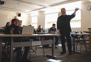 Professor Tom Bivins gestures to the front of the room while lecturing. 