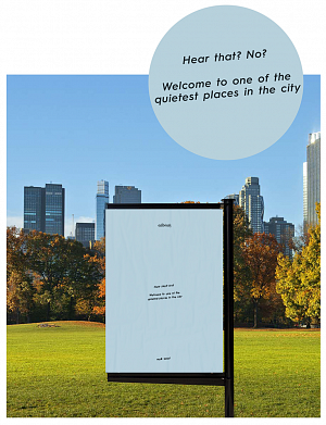 concept showing outdoor poster in a city park. The poster is blue and has small text that reads "Hear that? No? Welcome to one of the quietest places in the city."