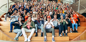dozens of people seated on a staircase display the O hand sign associated with the University of Oregon