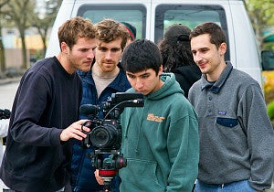 four people look into the viewfinder screen of a video camera