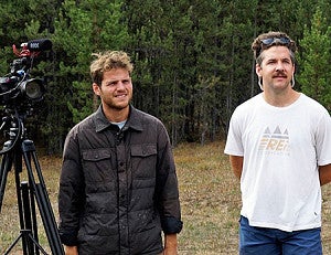 Sutton Raphael and Eric Straubhar stand in front of a forest with a video camera