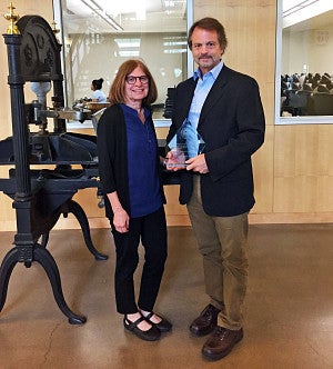 Leslie Steeves and Brent Walth, who is holding an award, stand on the second floor of Allen Hall