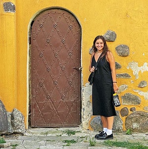 Sally Campbell stands by an old door on a crumbling bright yellow wall
