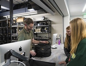Image shows two students at the J-Cage, checking out equipment from an SOJC staff member.