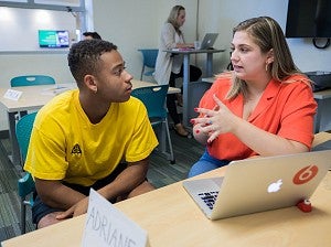 An SOJC writing coach works with a student in the Writing Lab. Both people are seated at a table, and a laptop is open in front of them. 