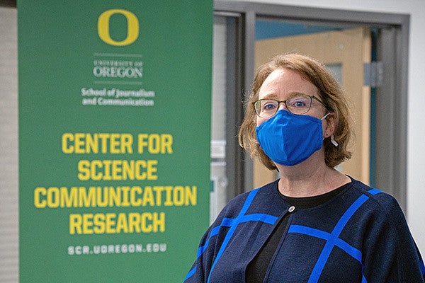 Ellen Peters wears a blue mask and stands in front of a banner that says Center for Science Communication Research