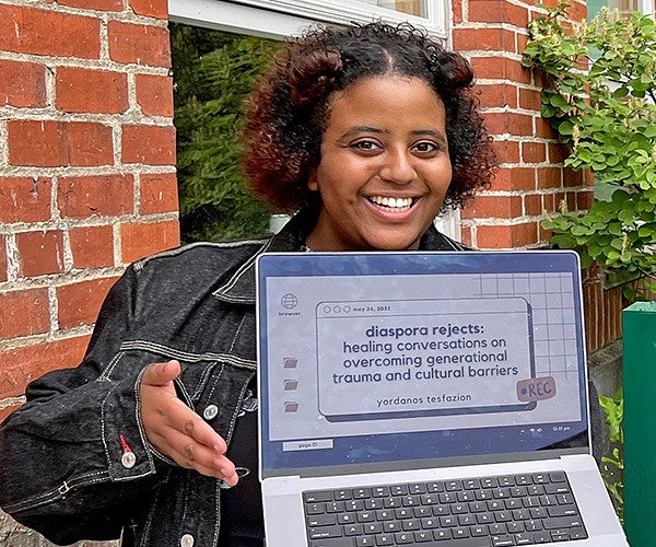Yordanos Tesfazion poses with a laptop in front of the Allen Hall sign on the University of Oregon campus