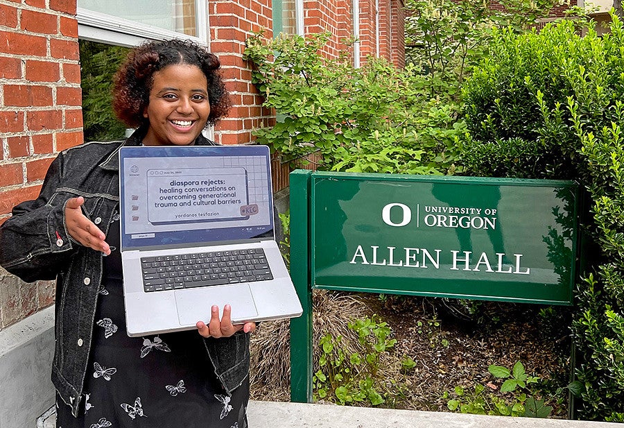 Yordanos Tesfazion poses with a laptop in front of the Allen Hall sign on the University of Oregon campus