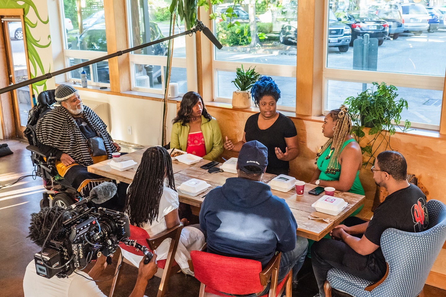 A group of Black Portlanders have a discussion around a table while they are filmed and recorded