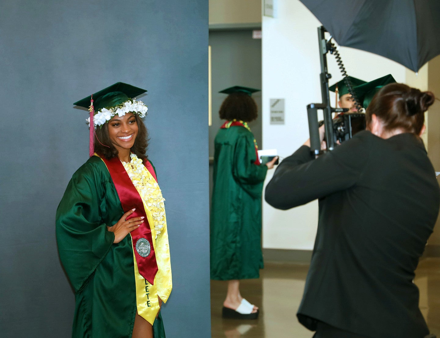 an SOJC graduate wearing a green cap and gown and a burgundy stole poses for a portrait at commencement